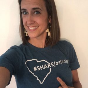 Lindsey, young brunette woman, points to her shirt which reads #SHAREfostering