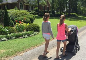 Tween girls, brunette, push a stroller in a neighborhood.
