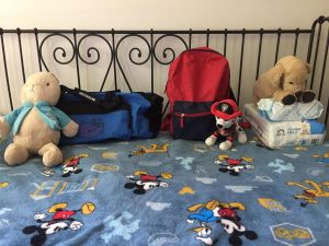 Bed with Mickey Mouse bedspread with three bags and stuffed animals.