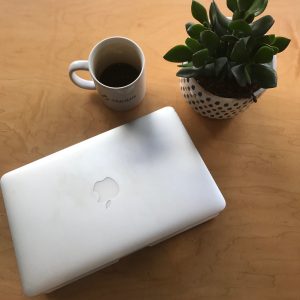 Table with coffee cup, laptop computer, and potted plant