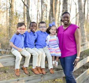 A young black woman stands with her four young children: 3 boys and one girl
