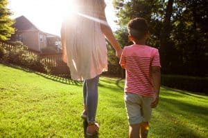 a teen girl holds hands with a young boy as they walk into sunlight.