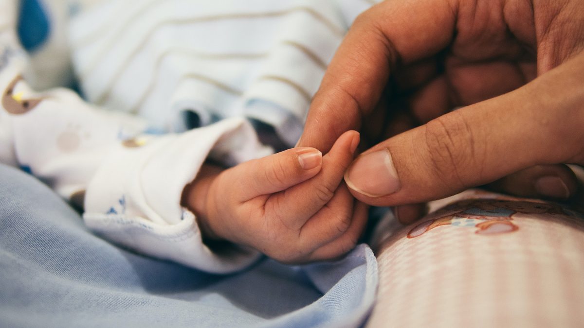adult hand holds newborn hand