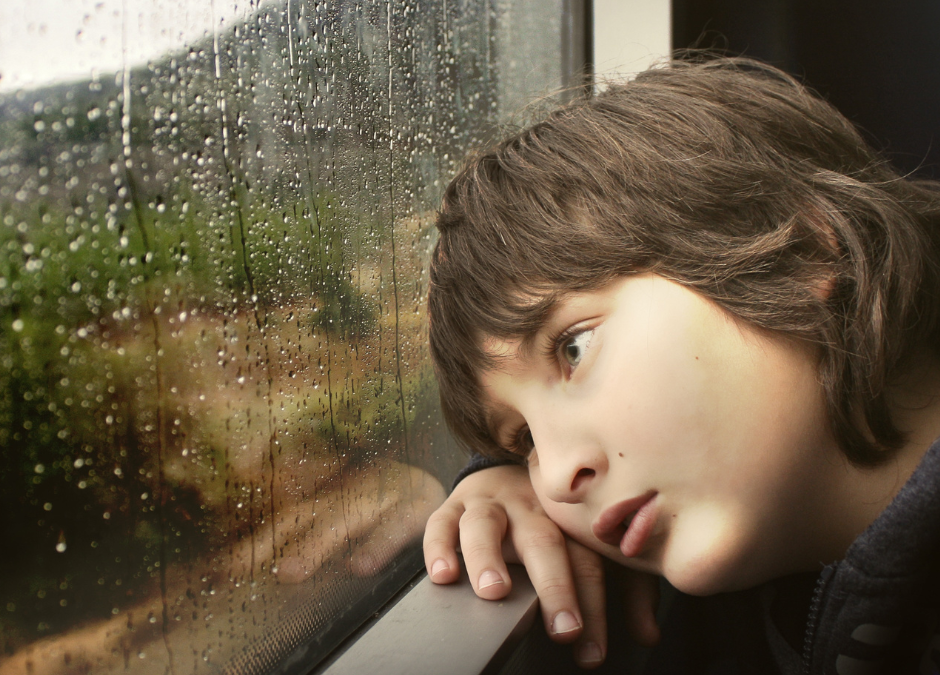 young boy staring out of rainy window