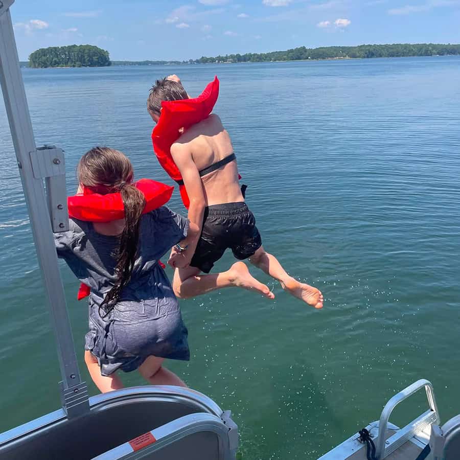 Brother and sister jumping off a boat into the lake